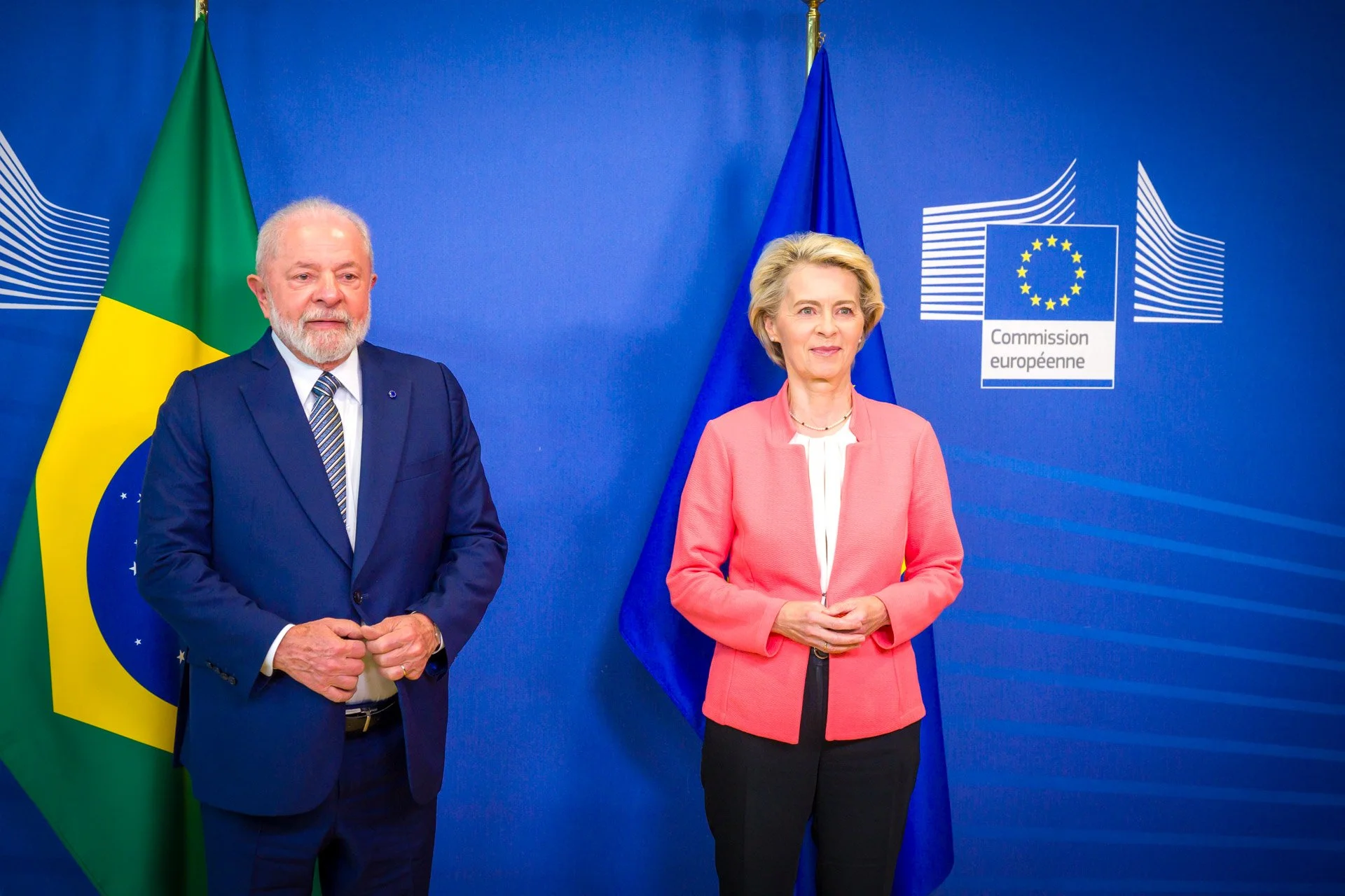 Deux personnes posent devant les drapeaux du Brésil et de l'Union européenne, avec un fond bleu et le logo de la Commission européenne.