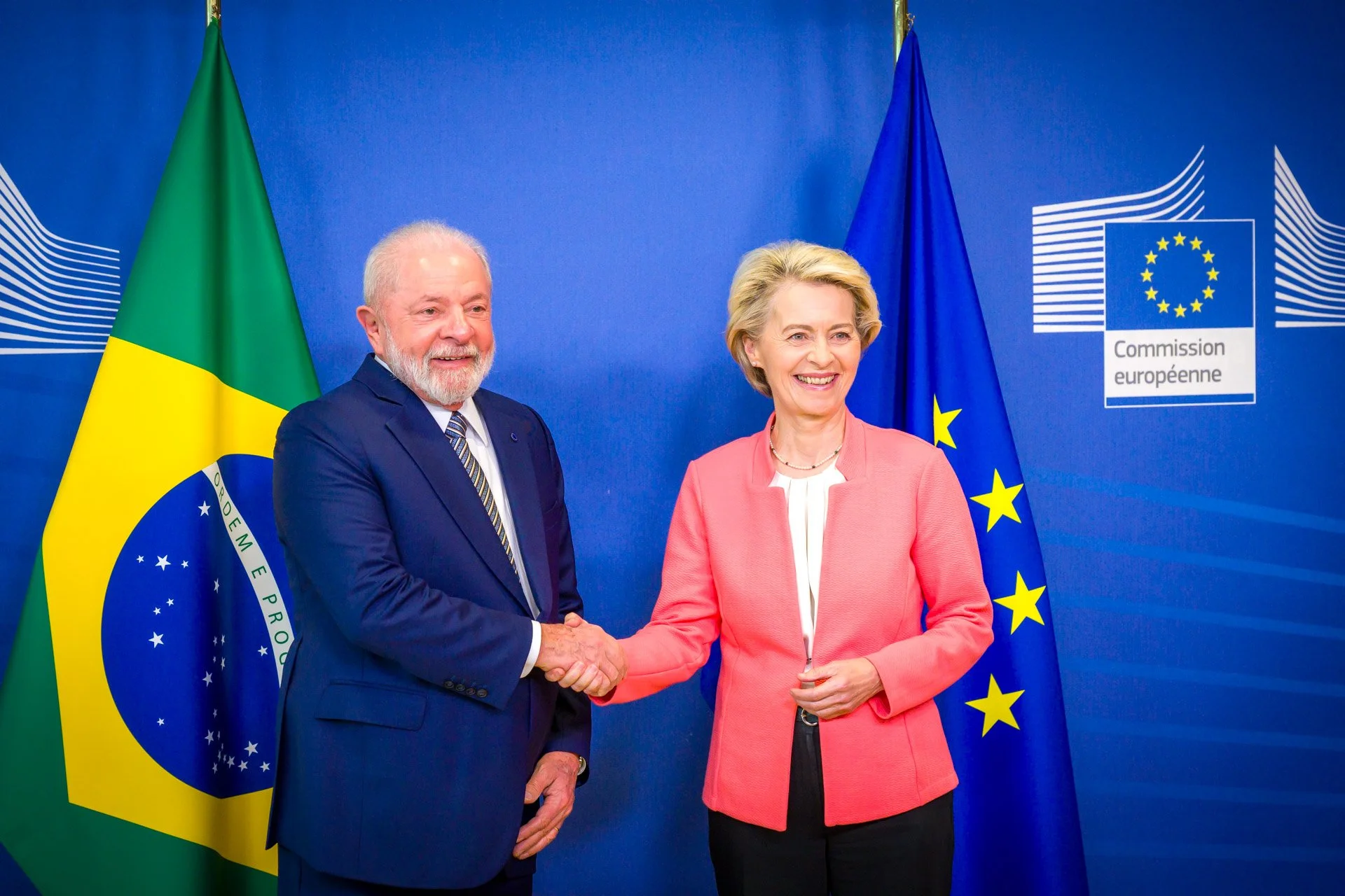 Deux personnes se serrant la main devant les drapeaux du Brésil et de l'Union européenne, avec un fond du logo de la Commission européenne.