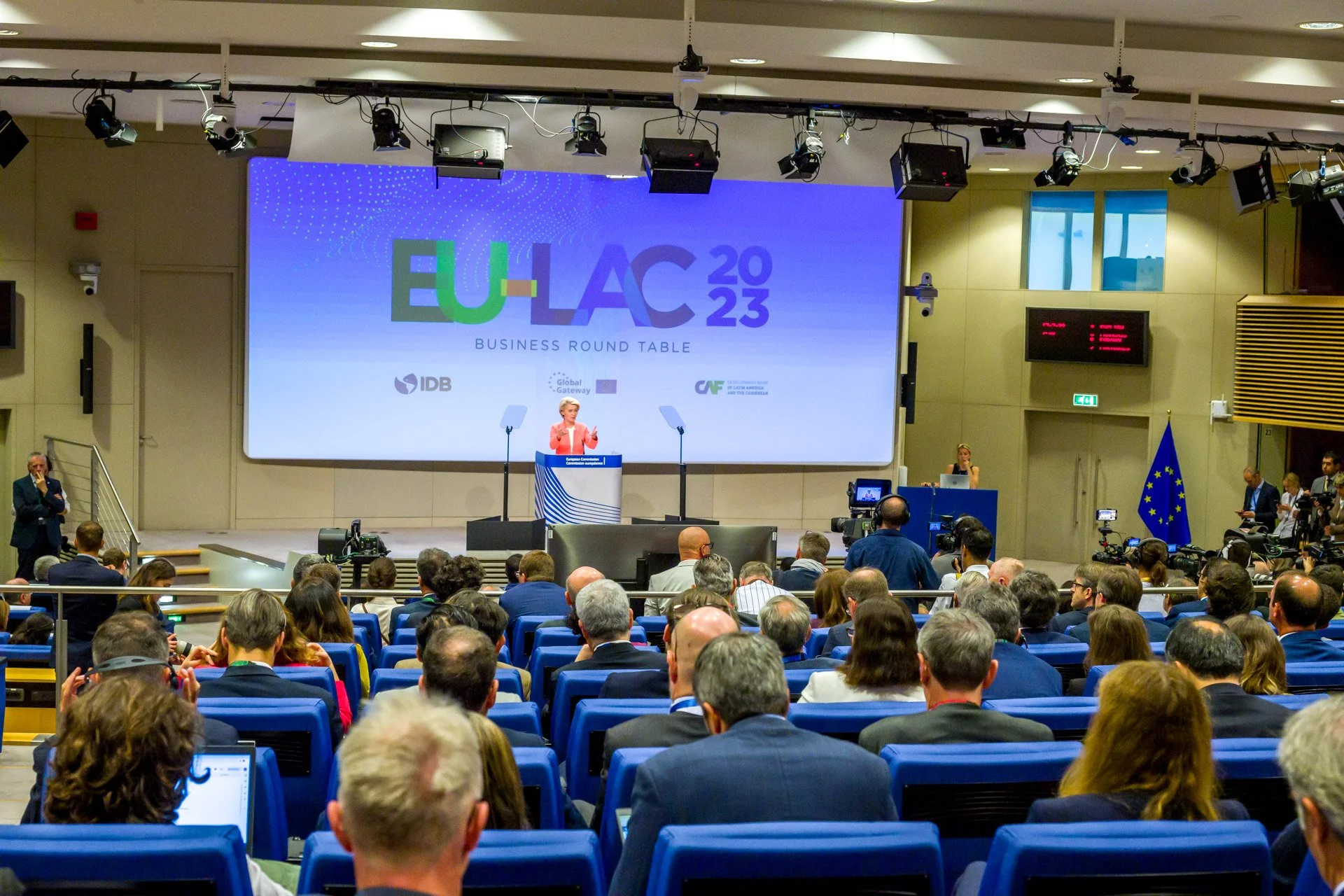 Conférence EU-LAC 2023 avec un orateur sur scène, public assis, et drapeau de l'UE, Bruxelles.
