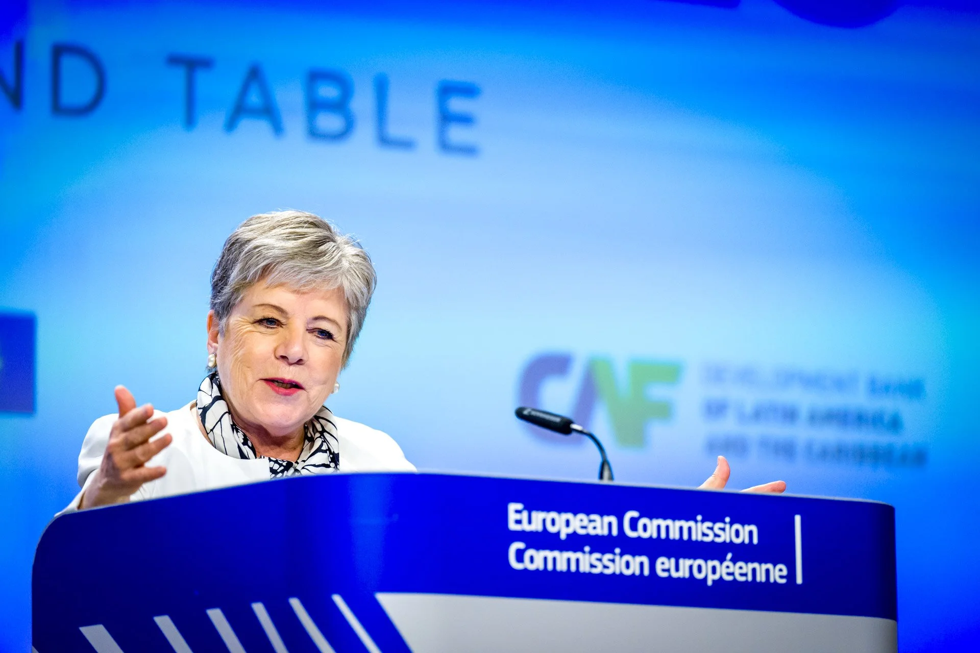 Une personne parle lors d'une conférence de presse de la Commission européenne, avec un logo "CAF" en arrière-plan.