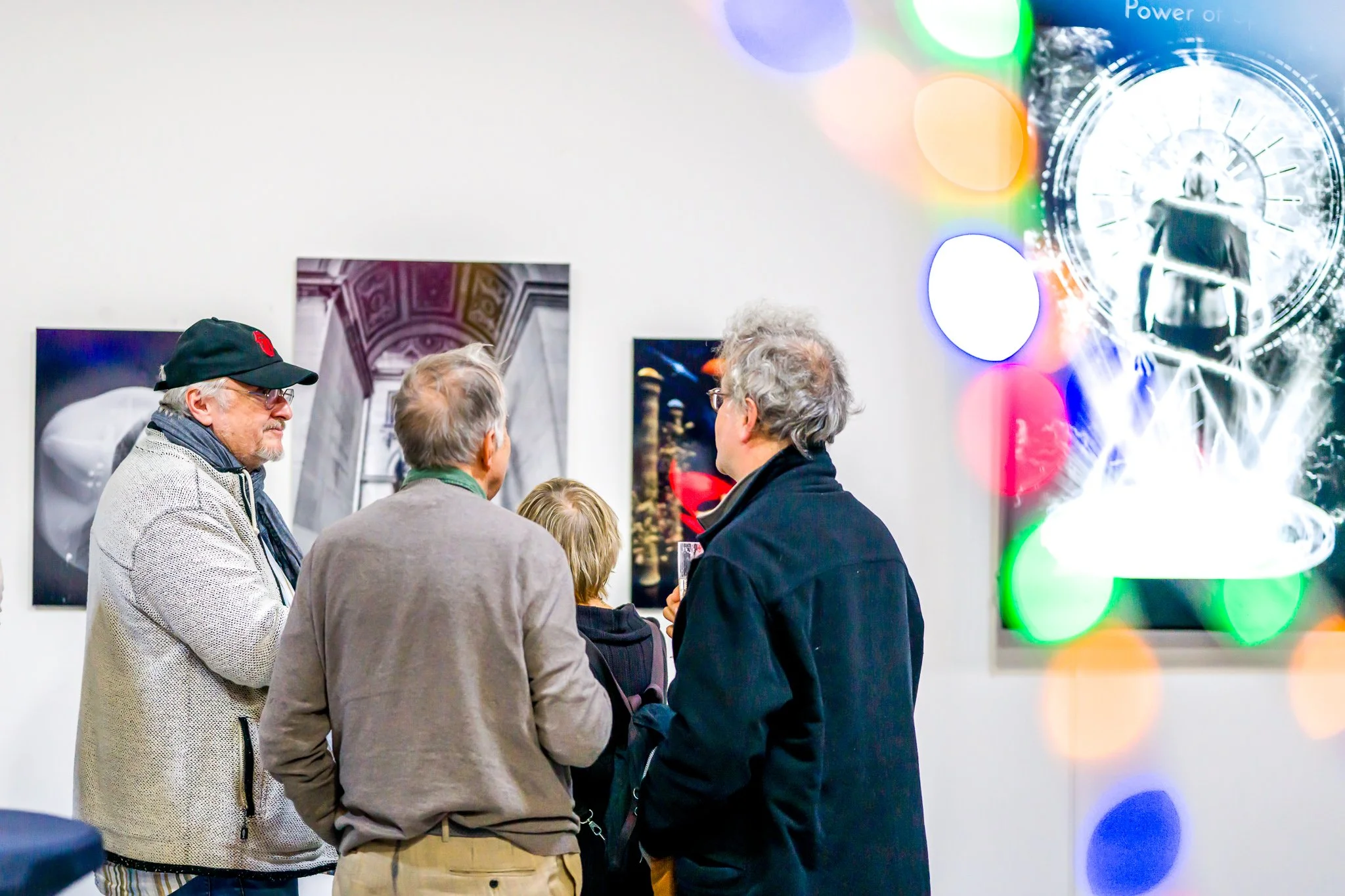 Des personnes regardant des œuvres d'art dans une galerie, avec des lumières colorées en premier plan.