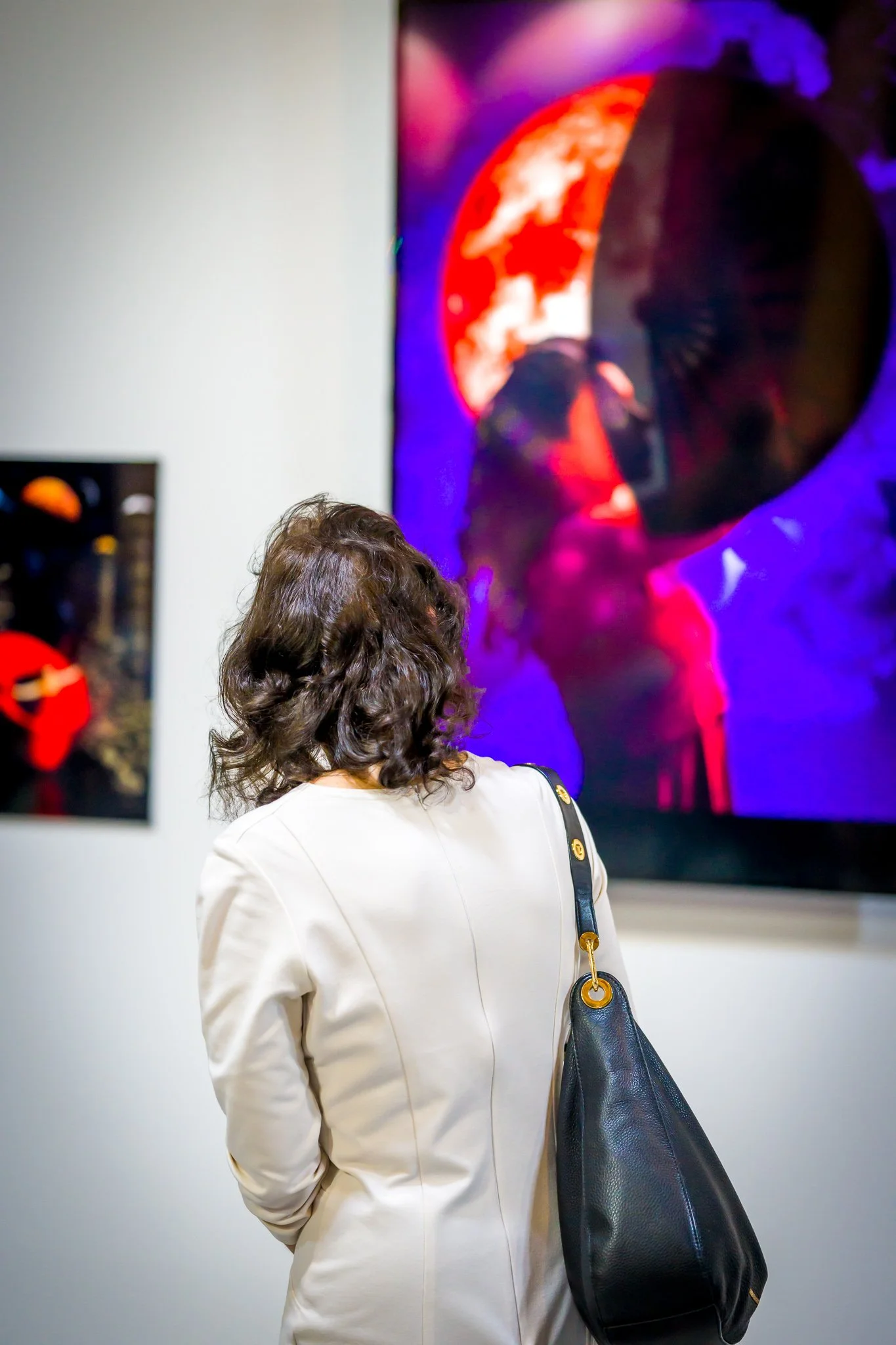 Une femme avec des cheveux bruns bouclés regarde une œuvre d'art colorée exposée dans une galerie.