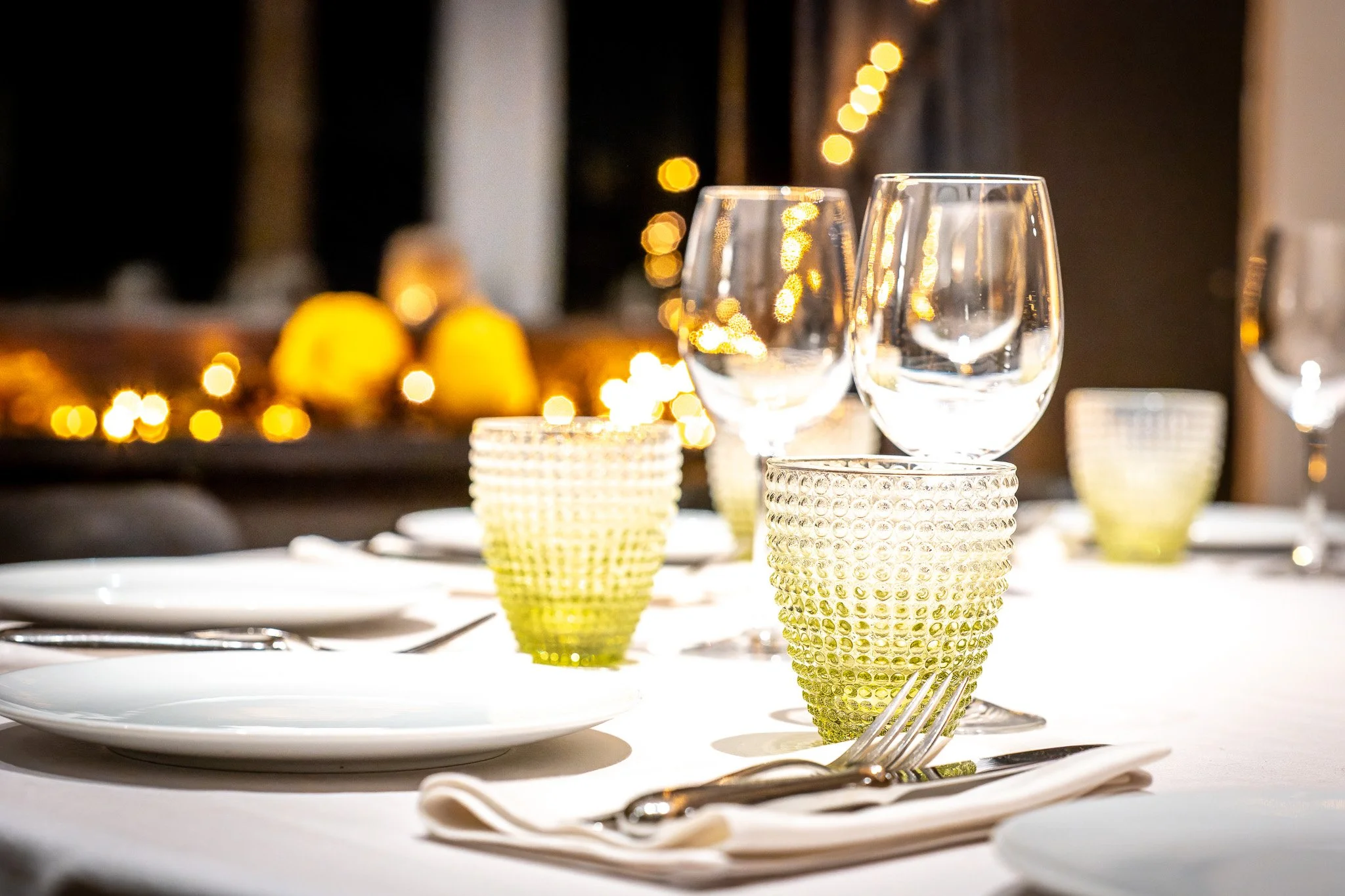 Photo d'un événement d'entreprise. Table de dîner élégante avec verres à vin, assiettes et verres texturés, lumières d'ambiance en arrière-plan.