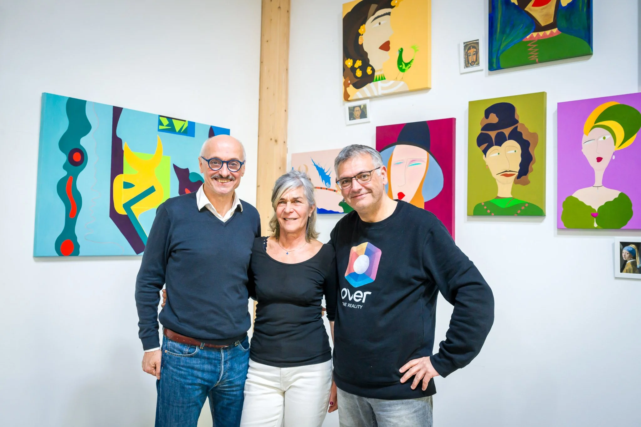 Trois personnes posant devant des peintures colorées sur un mur blanc.