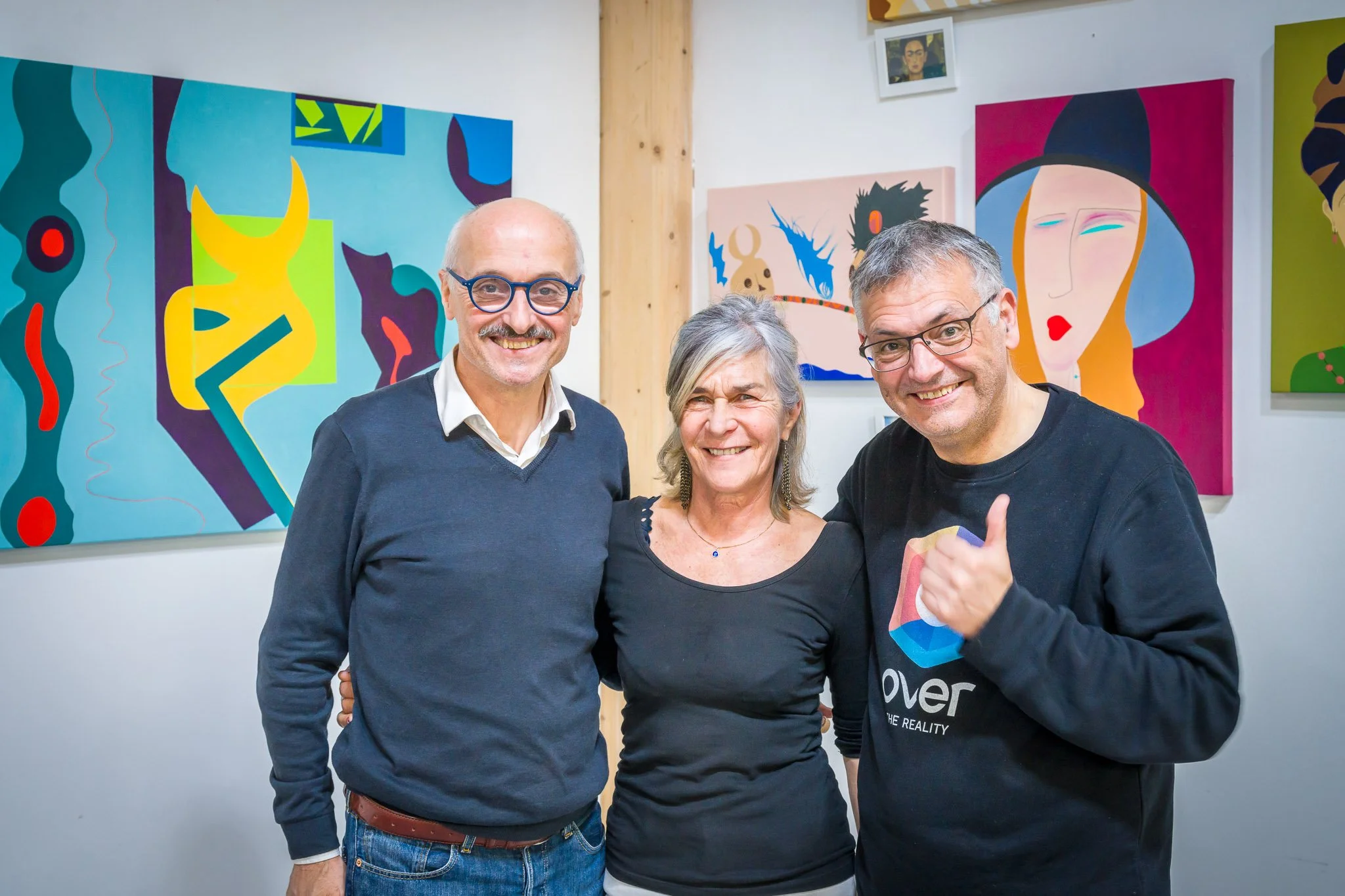Trois visiteurs souriants posent devant des tableaux colorés lors du vernissage de l’exposition d’Anne de Decker.