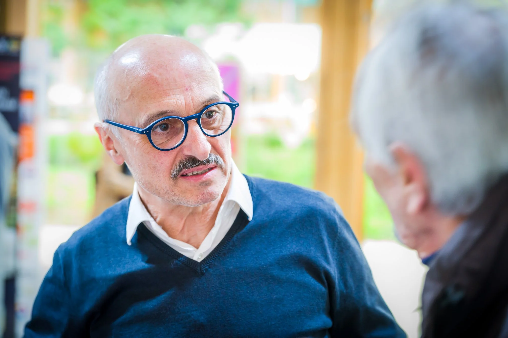 Deux hommes discutant, l'un portant des lunettes bleues.