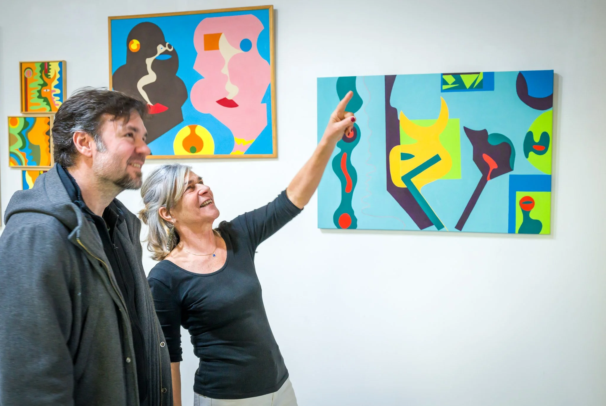 Deux personnes observent des peintures colorées et abstraites dans une galerie d'art.