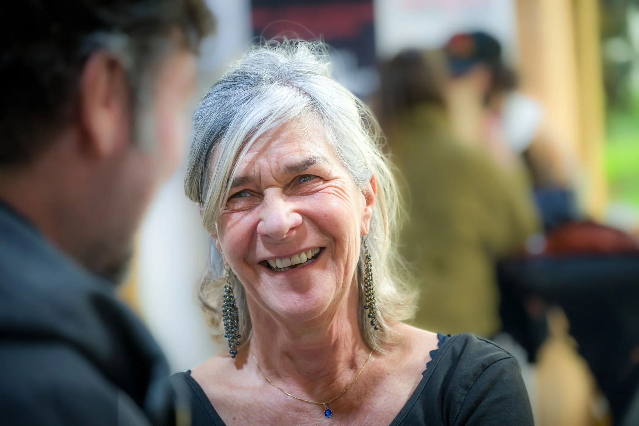Une visiteuse aux cheveux gris sourit à son interlocuteur lors du vernissage de l’exposition d’Anne de Decker.