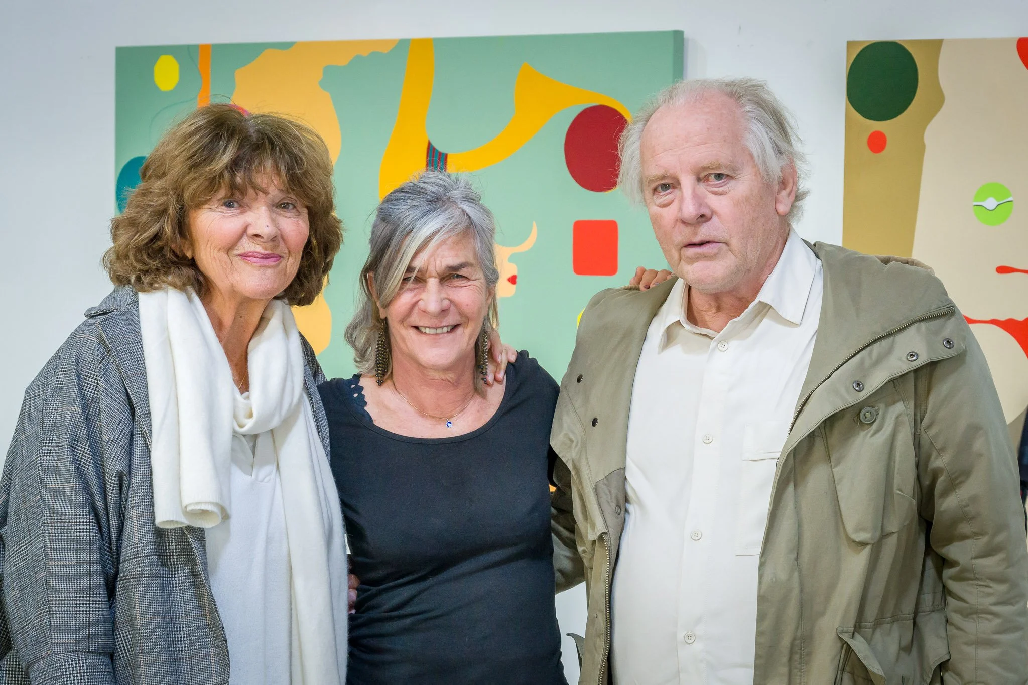 Trois personnes posant devant des œuvres d'art abstrait colorées.