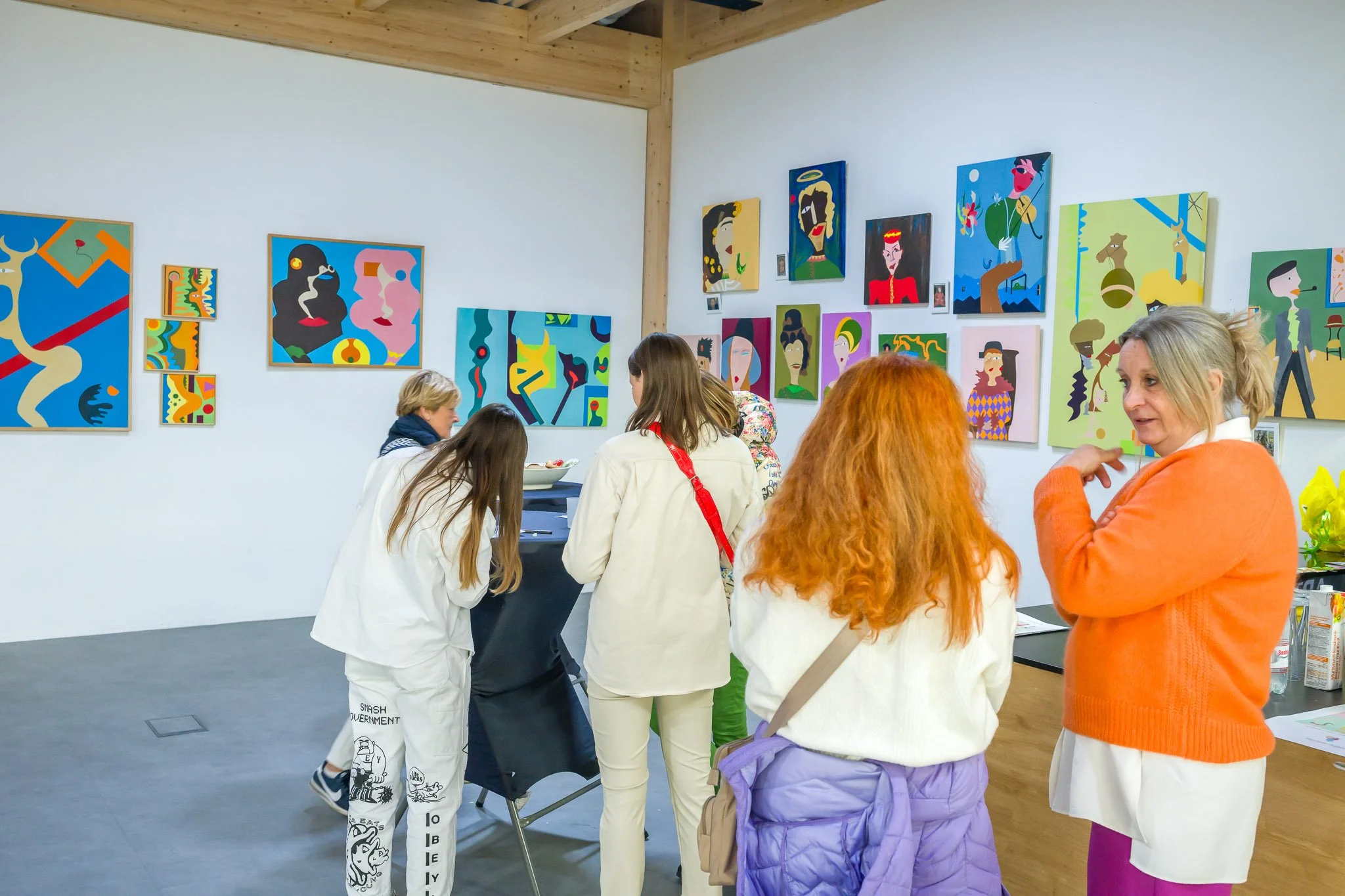 Photo événementielle pendant le vernissage d'une exposition. Des personnes dans une galerie d'art regardent des peintures colorées accrochées aux murs.