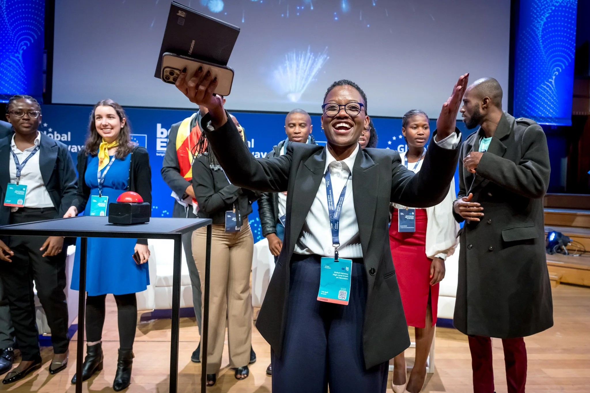 A group of people on stage at an event, with a woman enthusiastically holding aloft a trophy.