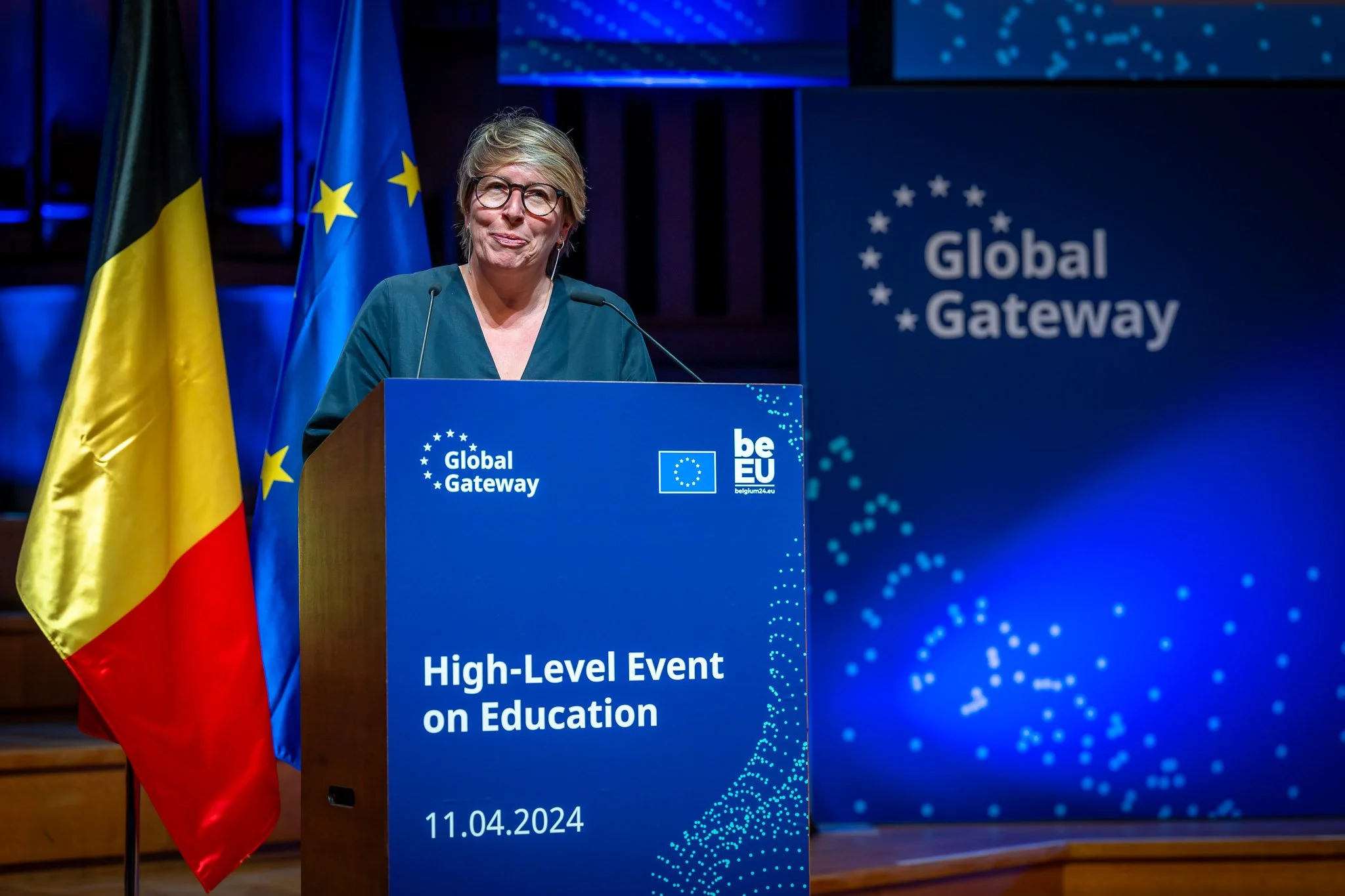 A person is giving a speech from behind a lectern at the Global Gateway’s “High-Level Event on Education”, with the flags of the European Union and Belgium in the background.