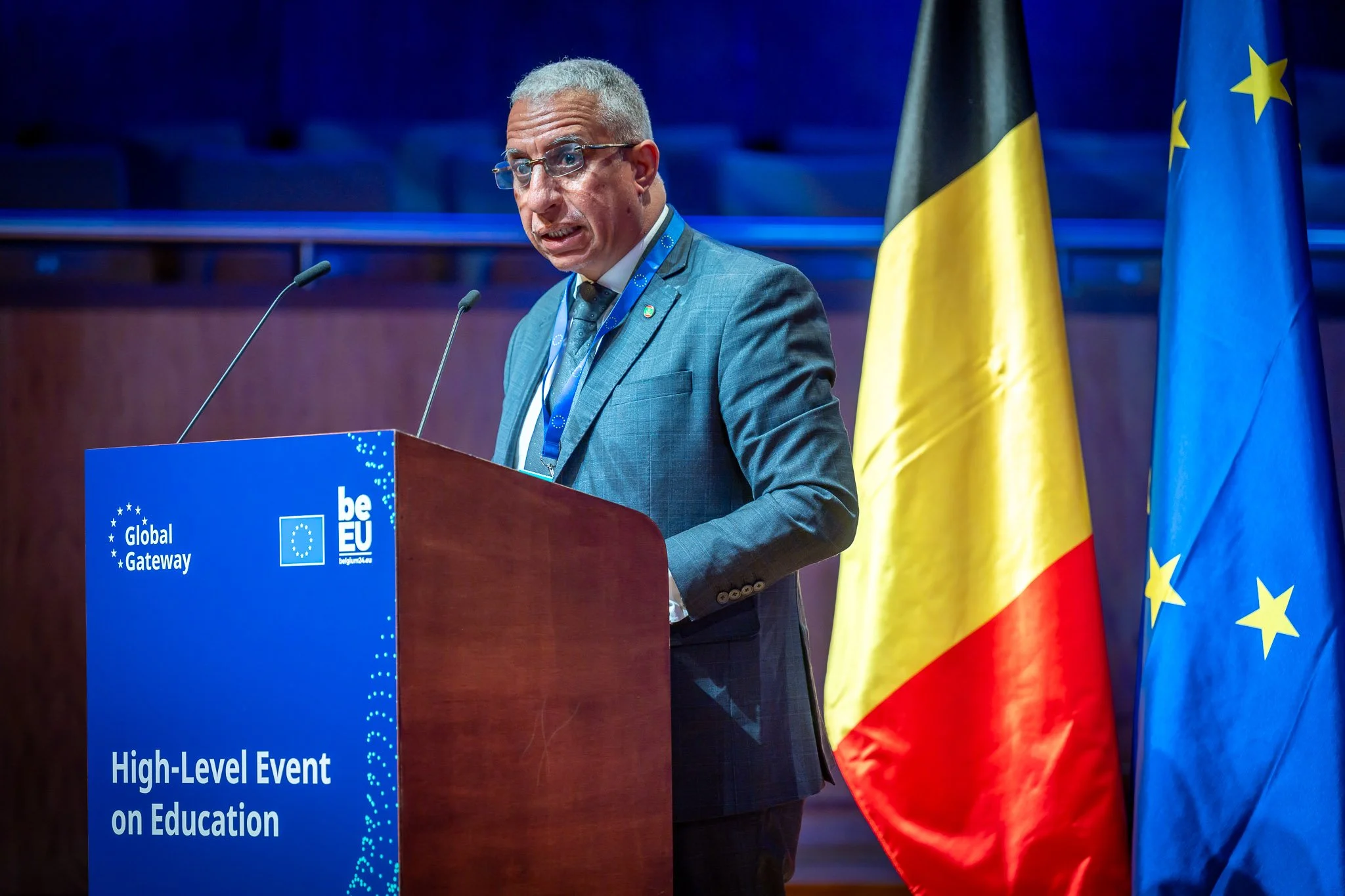 A man speaking at a podium during an event on education. There are Belgian and European Union flags in the background.