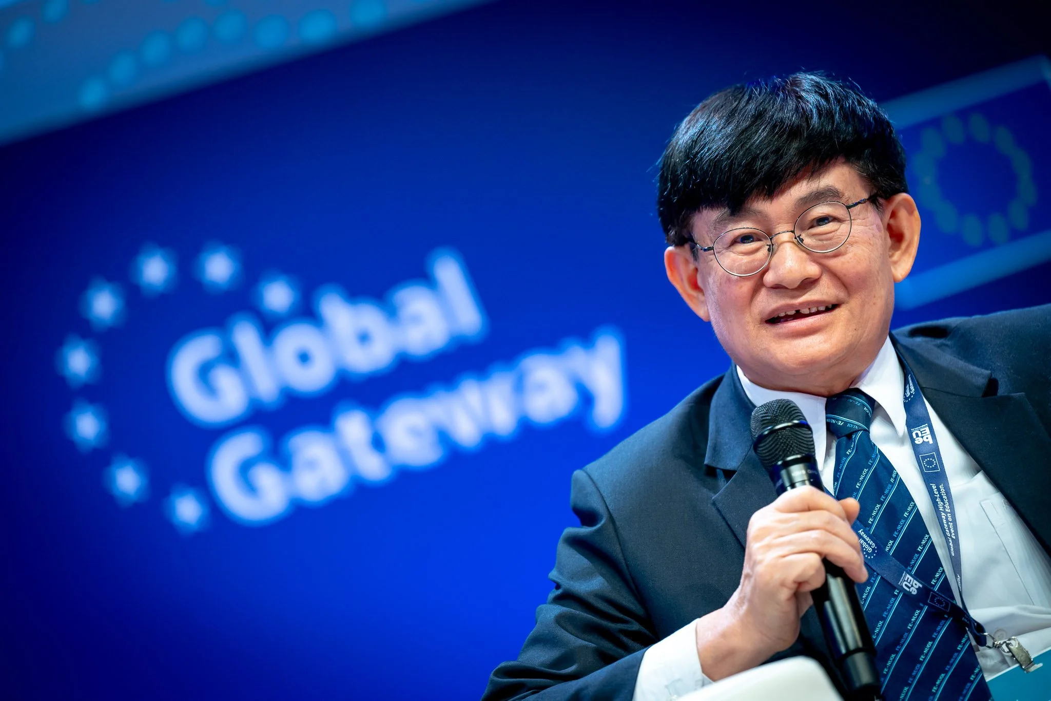 A man in a suit holding a microphone, standing in front of a sign reading ‘Global Gateway’.