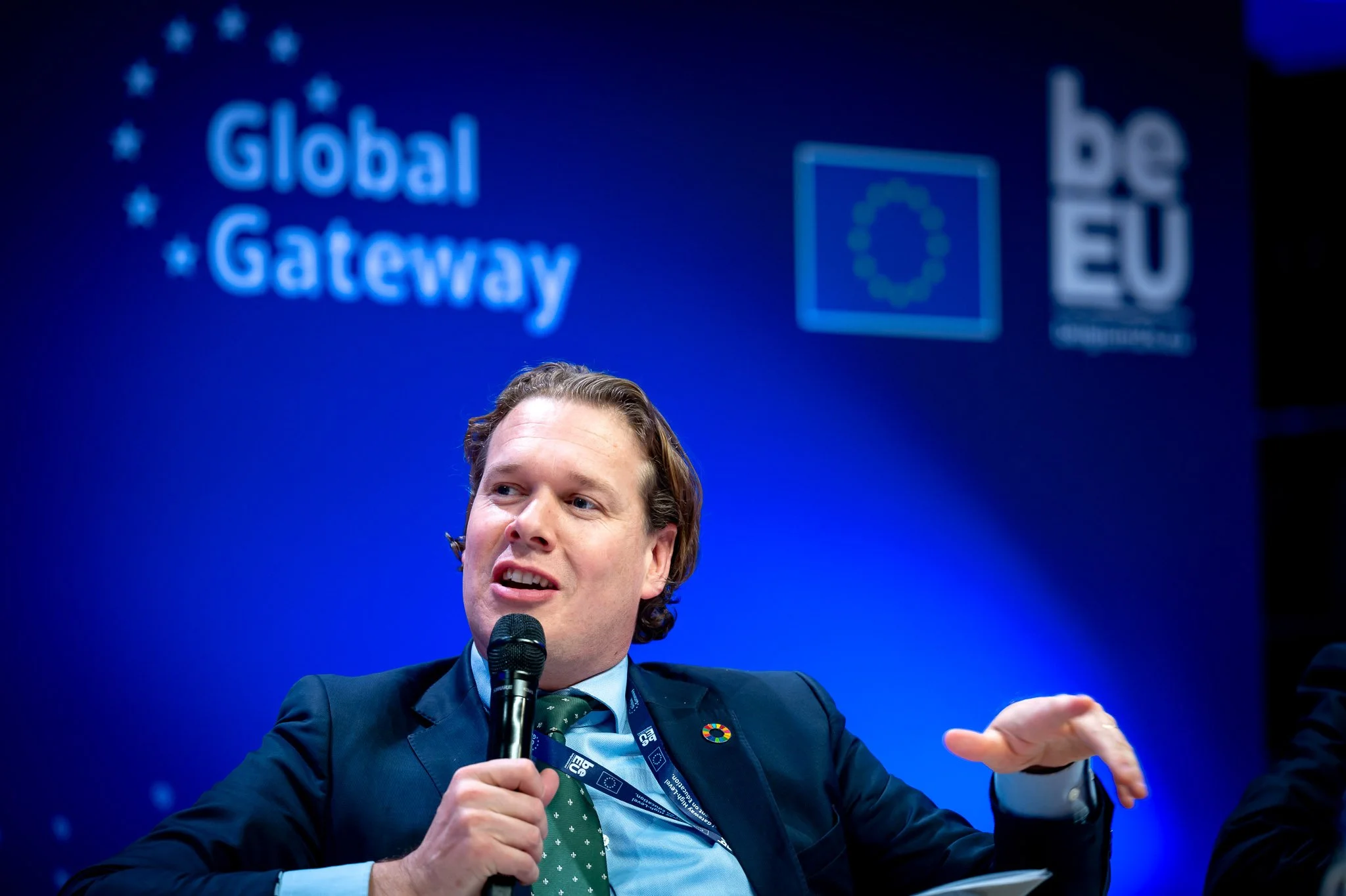 A man speaking into a microphone at a ‘Global Gateway’ event, against a blue background featuring European logos.