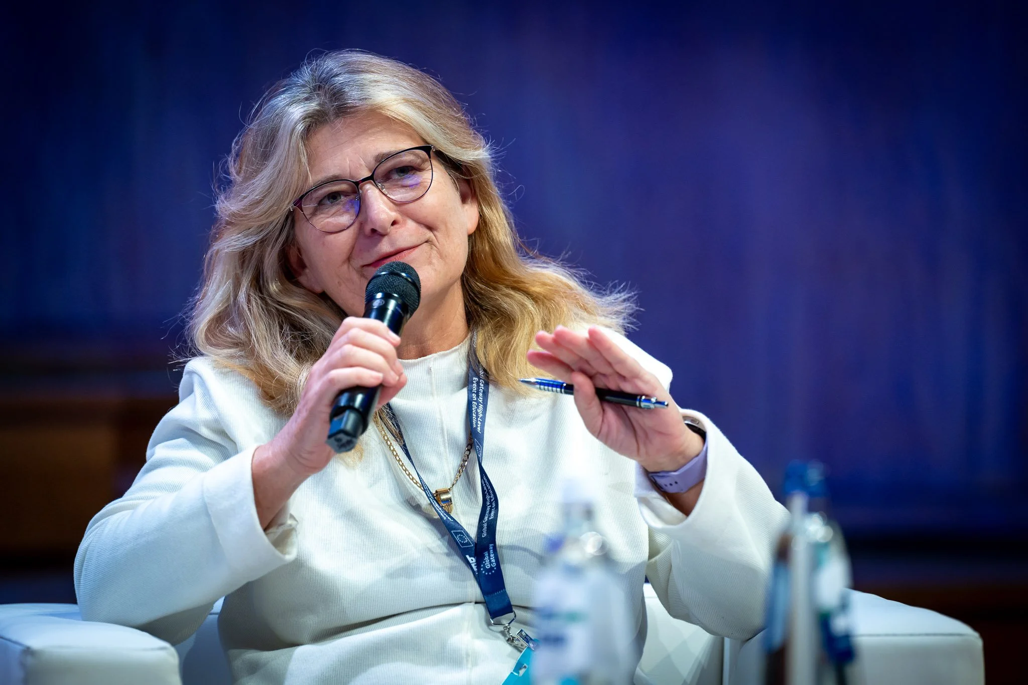 A woman wearing glasses, holding a microphone, taking part in a conference.