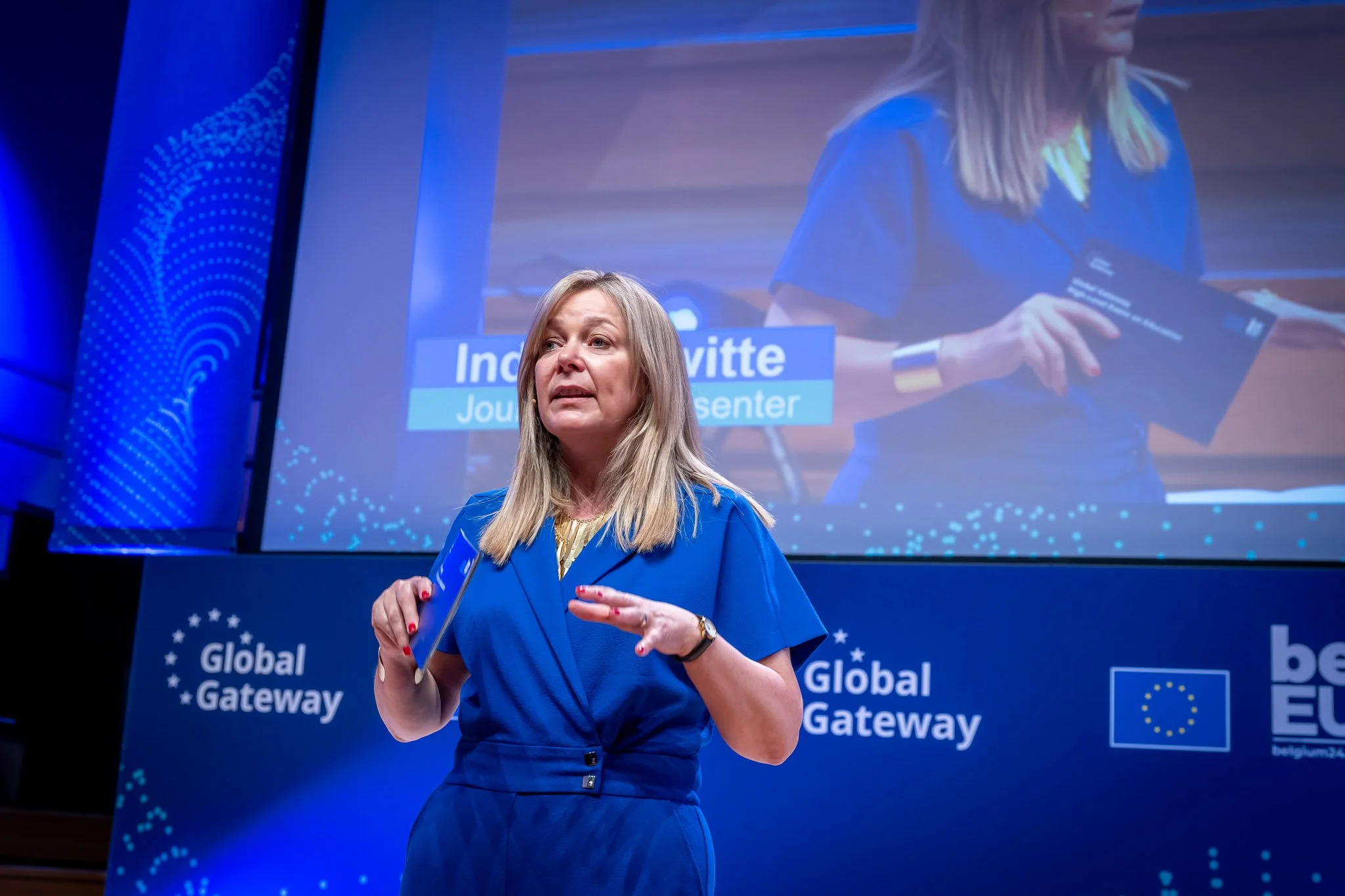 A woman in blue on stage at the Global Gateway event, with a screen in the background.
