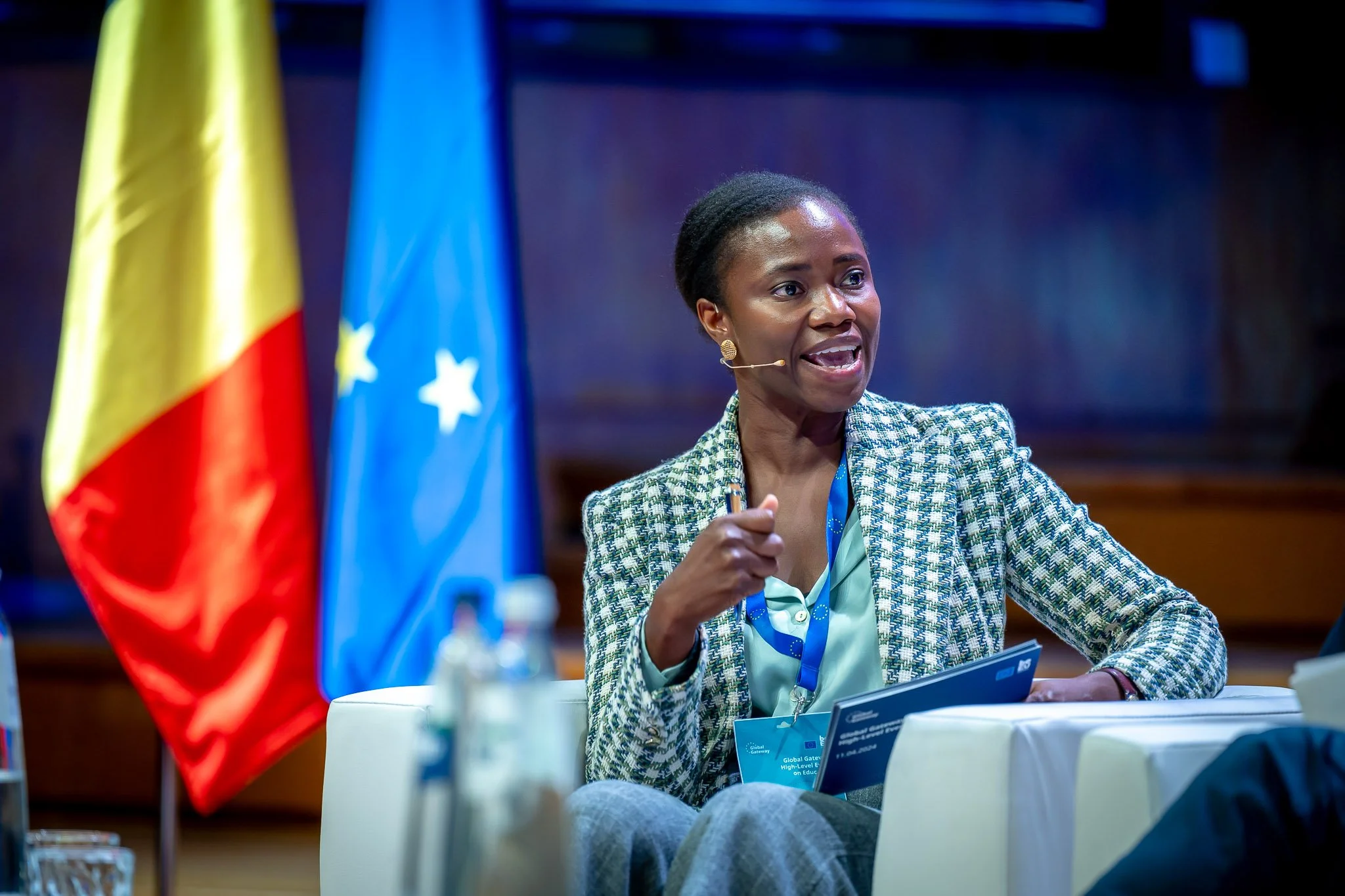 A woman speaking at a conference with flags in the background.