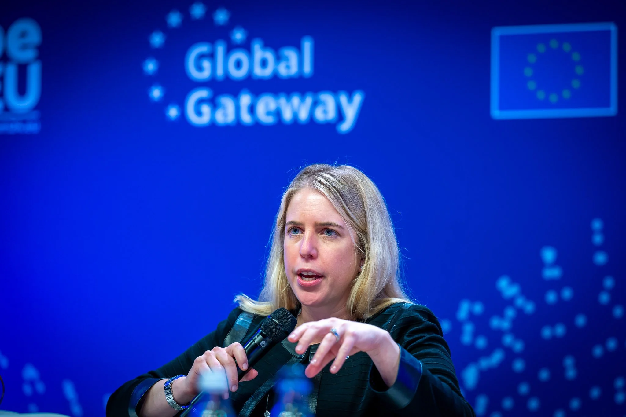 A person holding a microphone at a ‘Global Gateway’ event, with a blue background and EU logos.