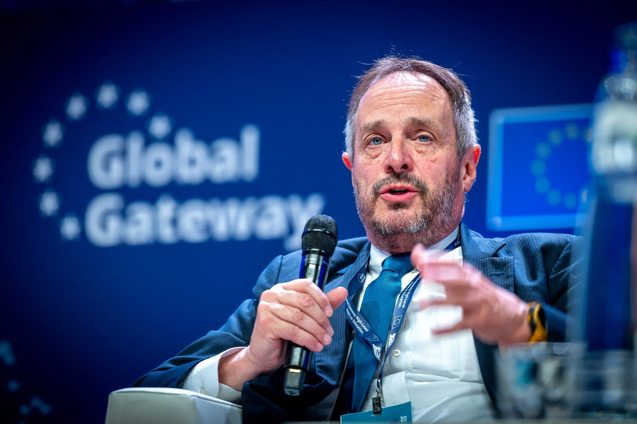 A man in a suit and tie is speaking into a microphone at an event called “Global Gateway”, against a blue backdrop displaying European Union logos.