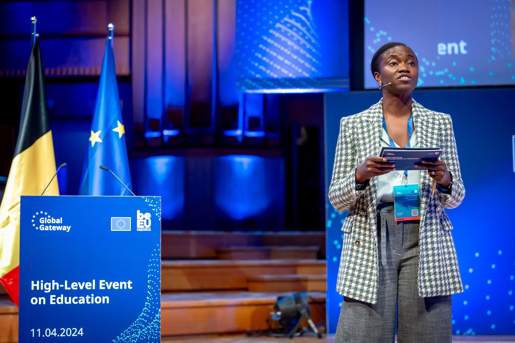 A speaker at an educational event in 2024, with the flags of the European Union and Belgium in the background.