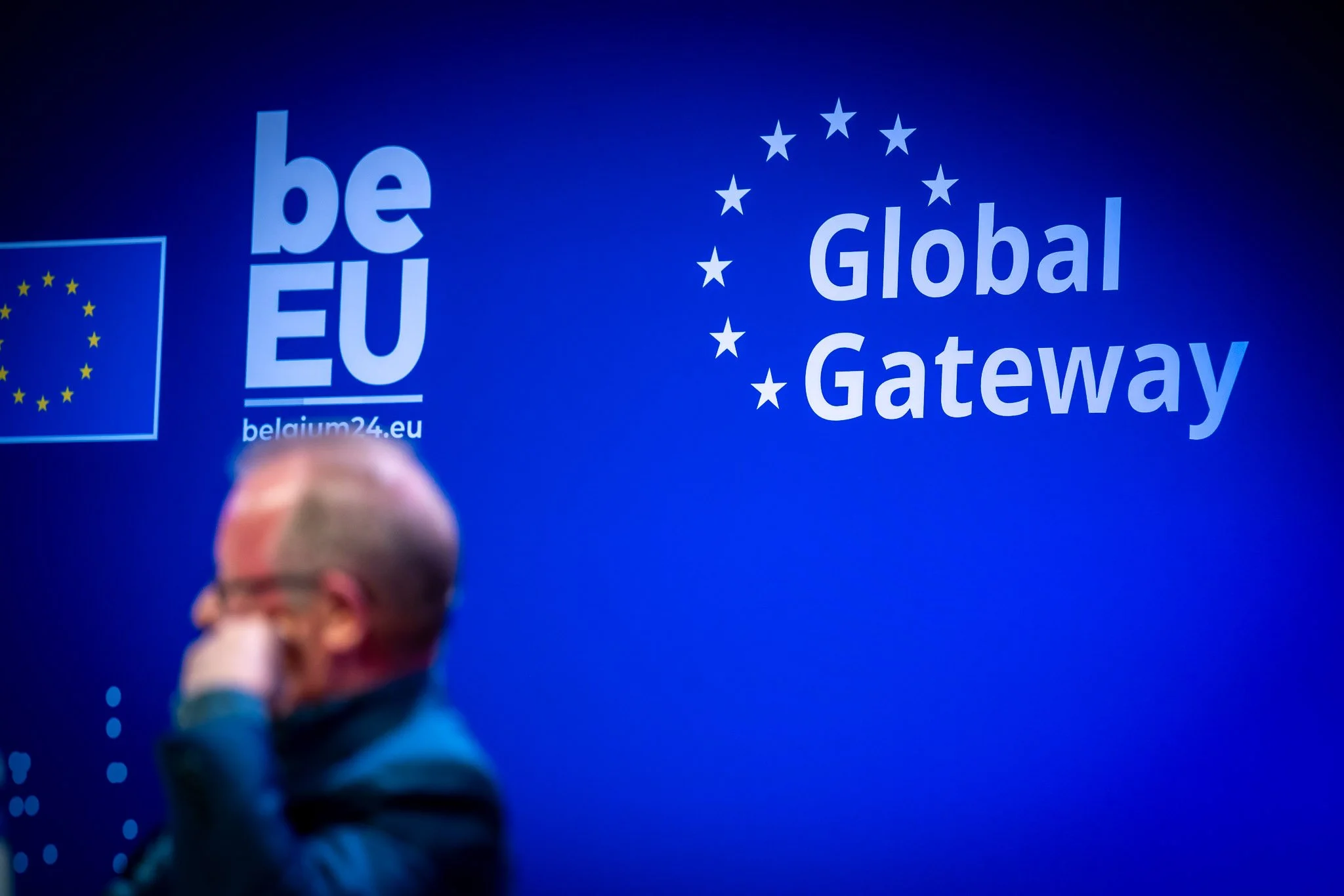A blue background featuring the European Union’s “beEU” and “Global Gateway” logos, with a blurred figure of a man in the foreground.