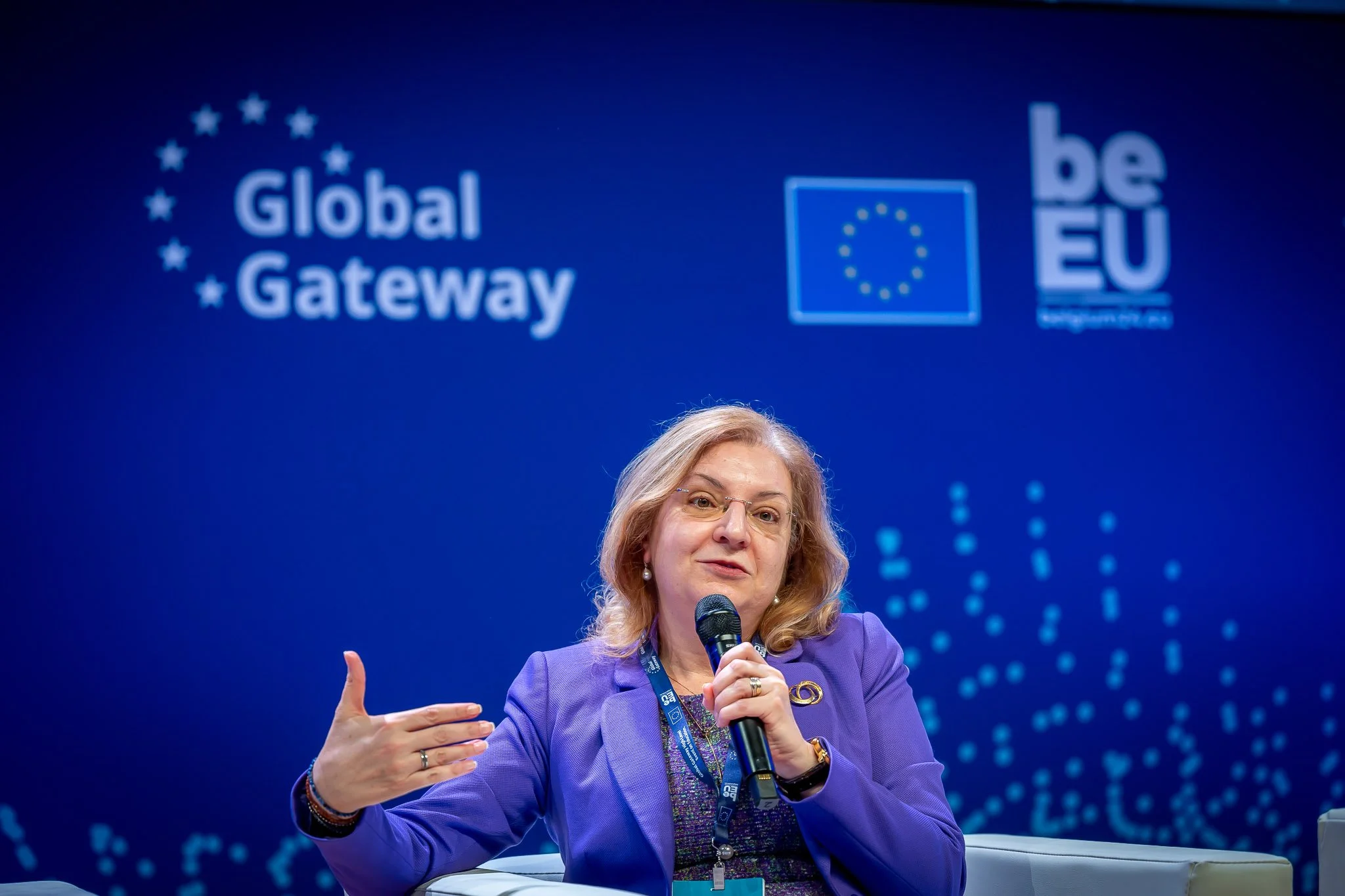 A woman holding a microphone at a ‘Global Gateway’ event, with the EU logo in the background.