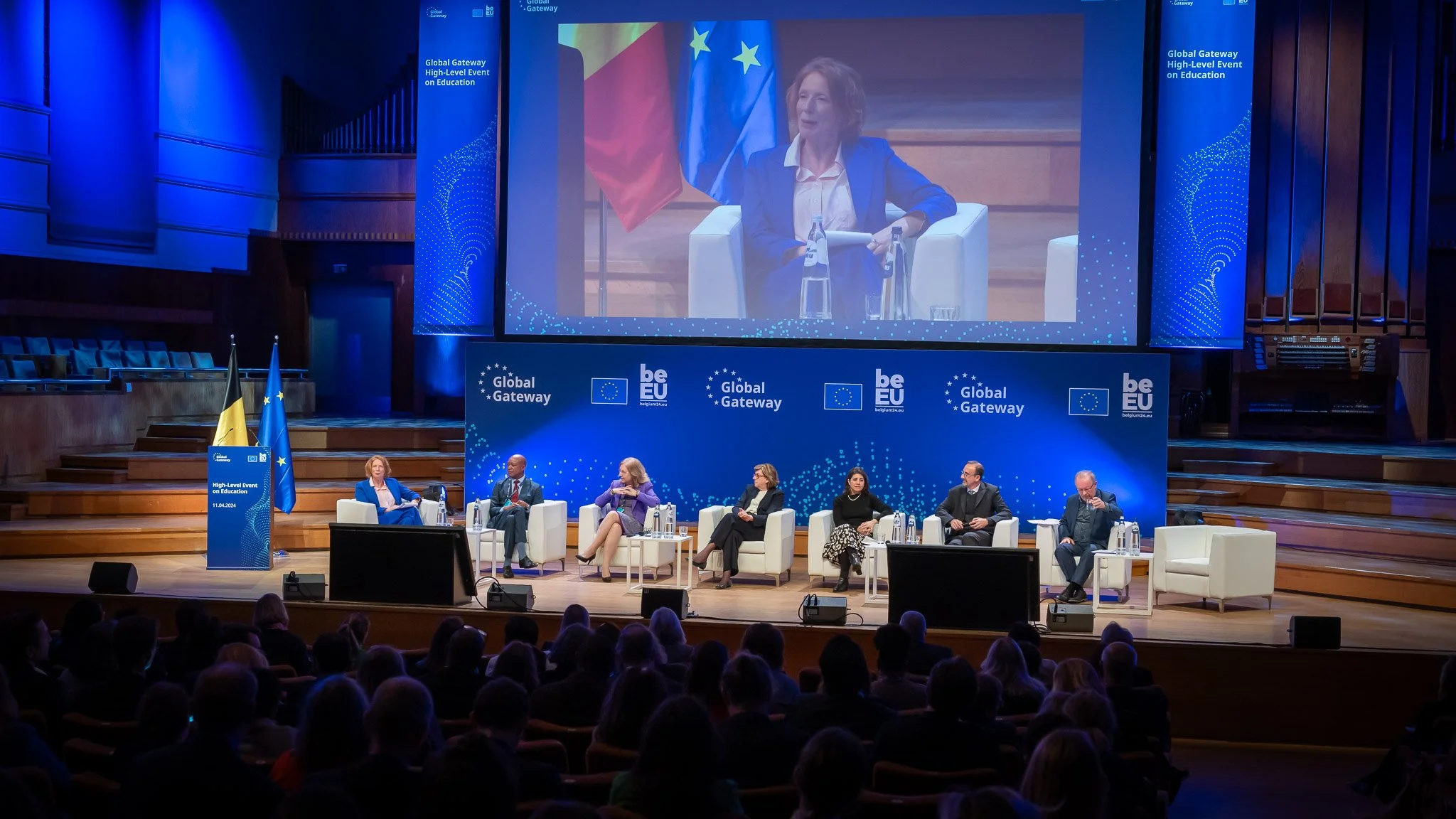 Global Gateway high-level conference on education, with several speakers seated on stage, the audience in the foreground, European flags and a blue background.
