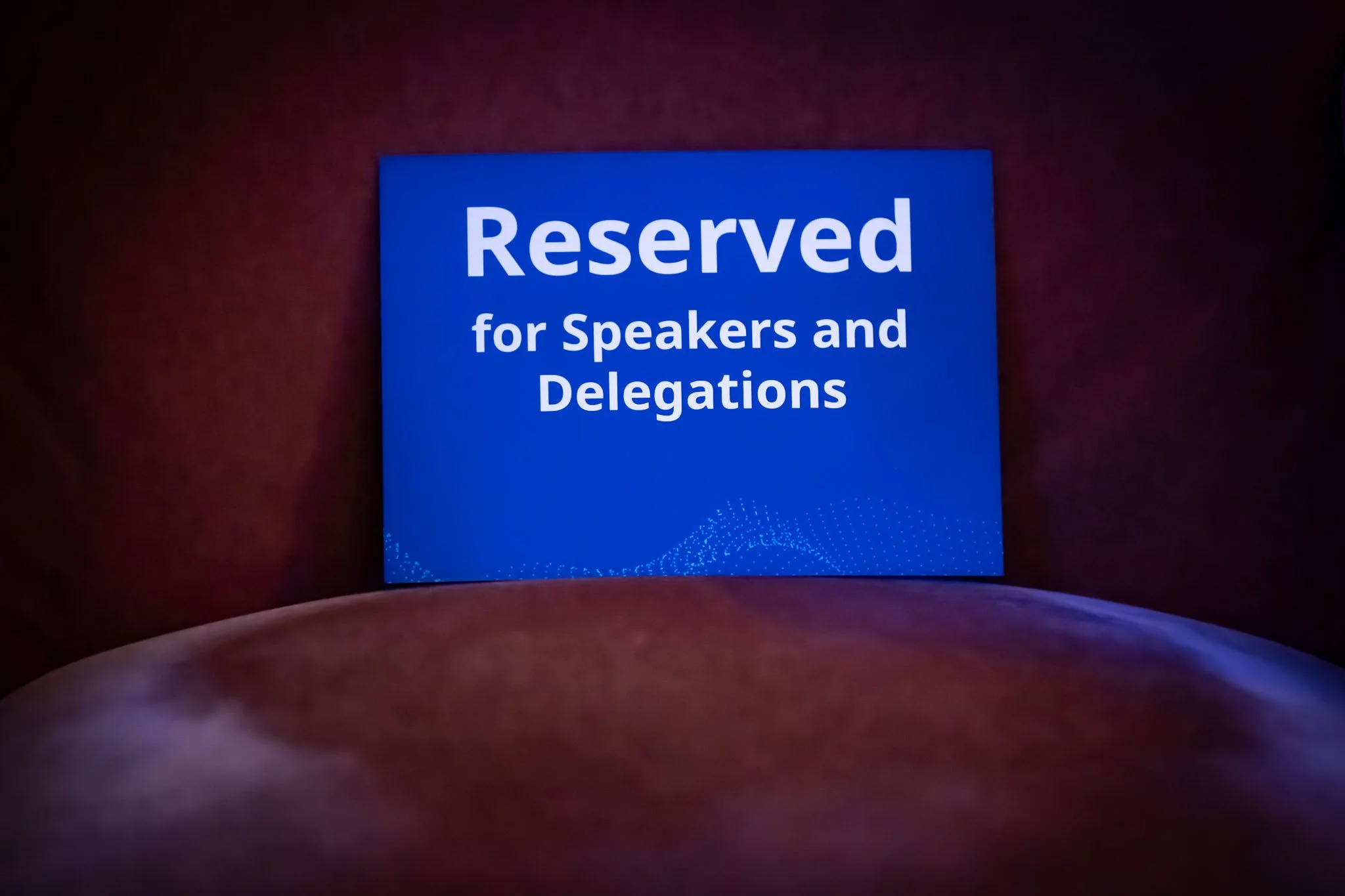 Panneau bleu affichant 'Reserved for Speakers and Delegations' dans une salle sombre.