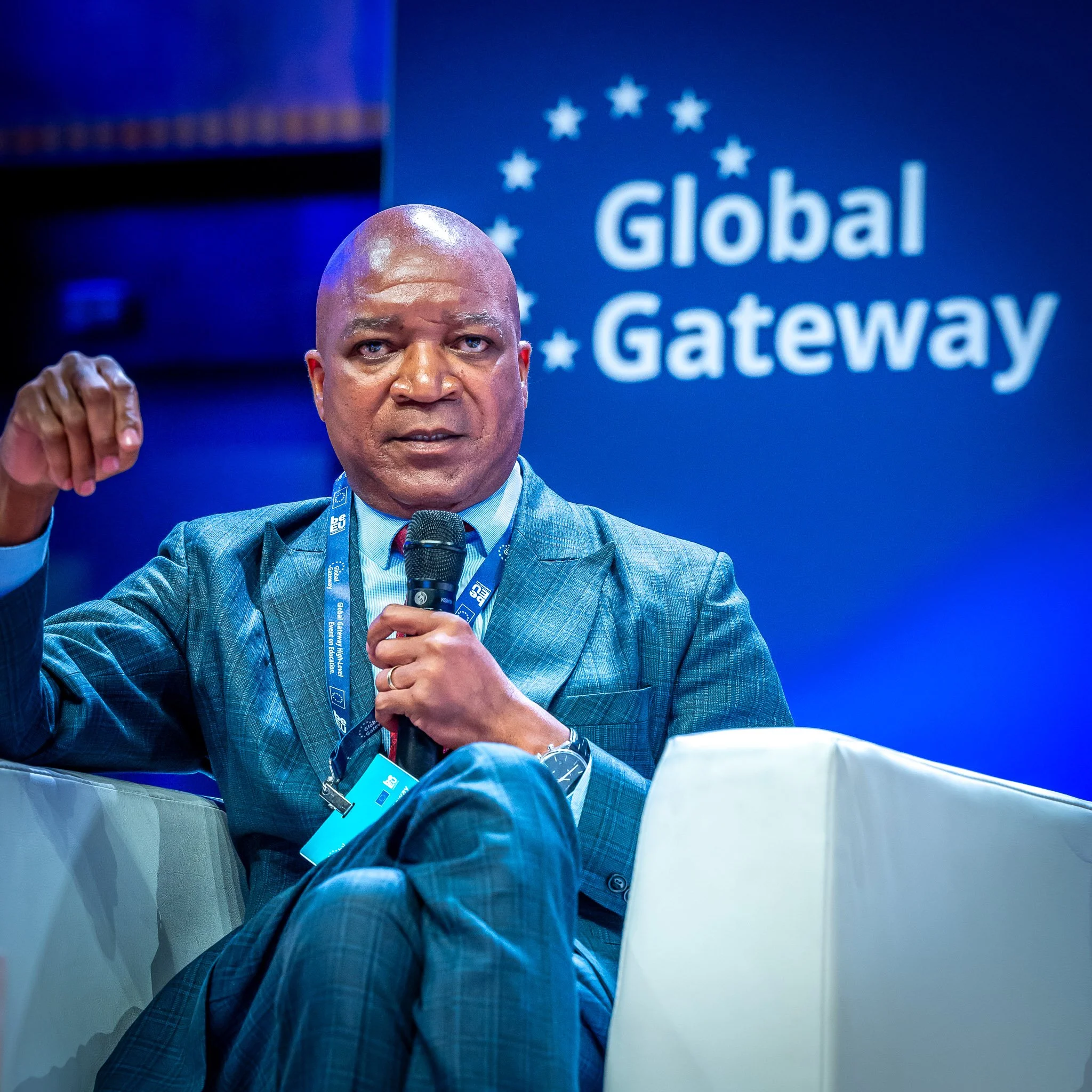 A man in a blue suit holding a microphone, seated at an event with the ‘Global Gateway’ sign in the background.