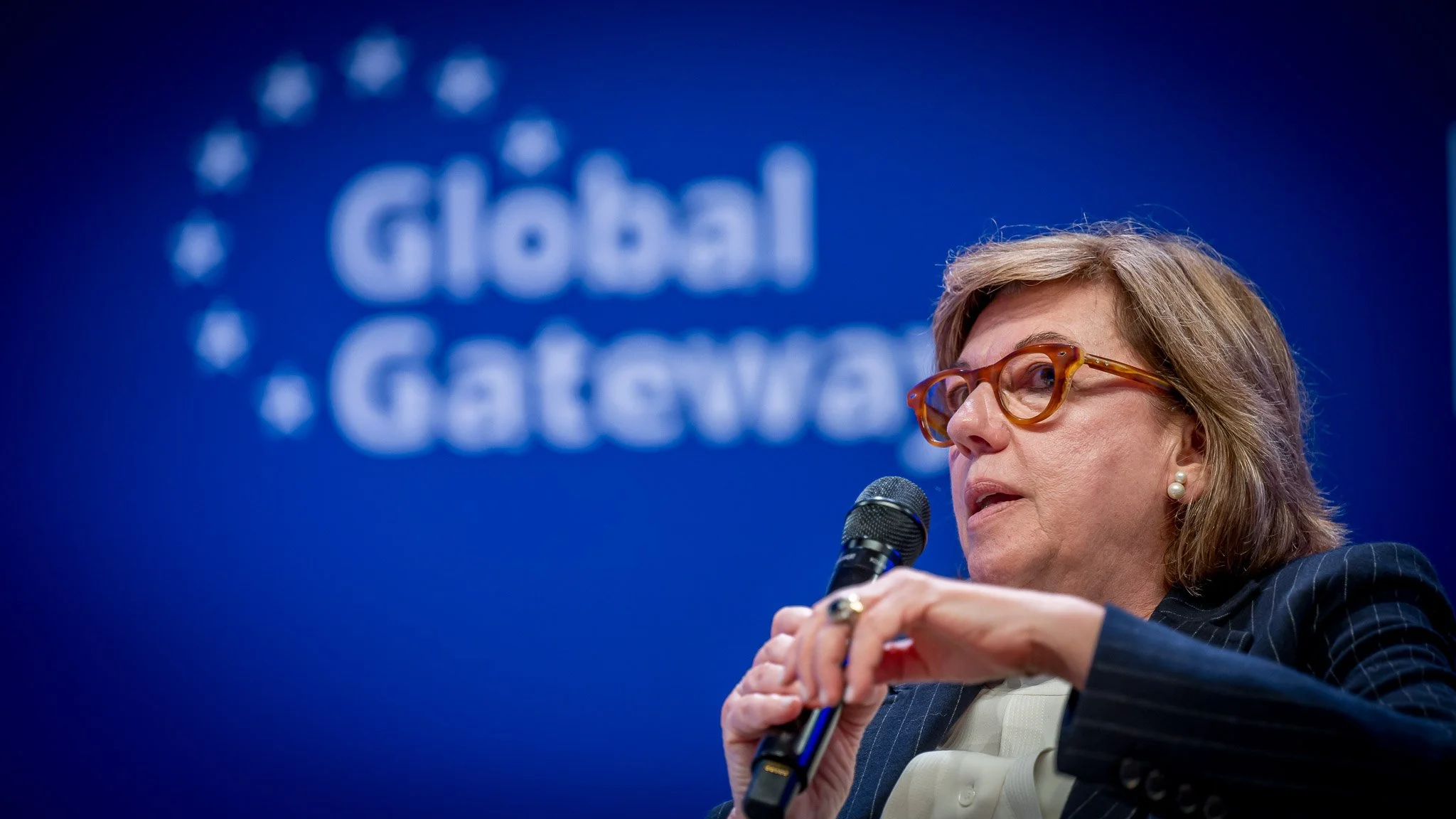 A woman holding a microphone, against a blue background with the text ‘Global Gateway’.