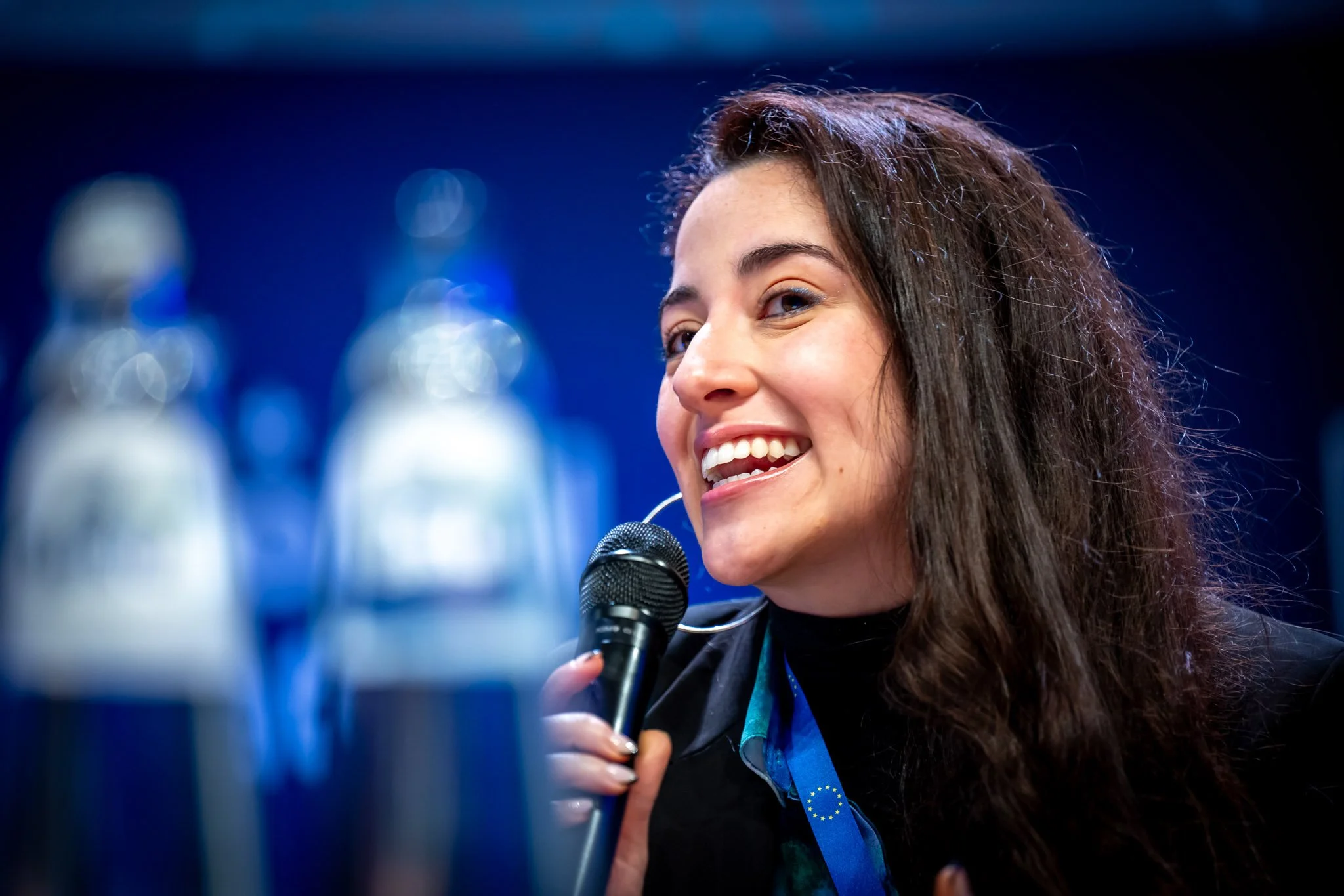 A smiling woman holding a microphone against a blurred background.