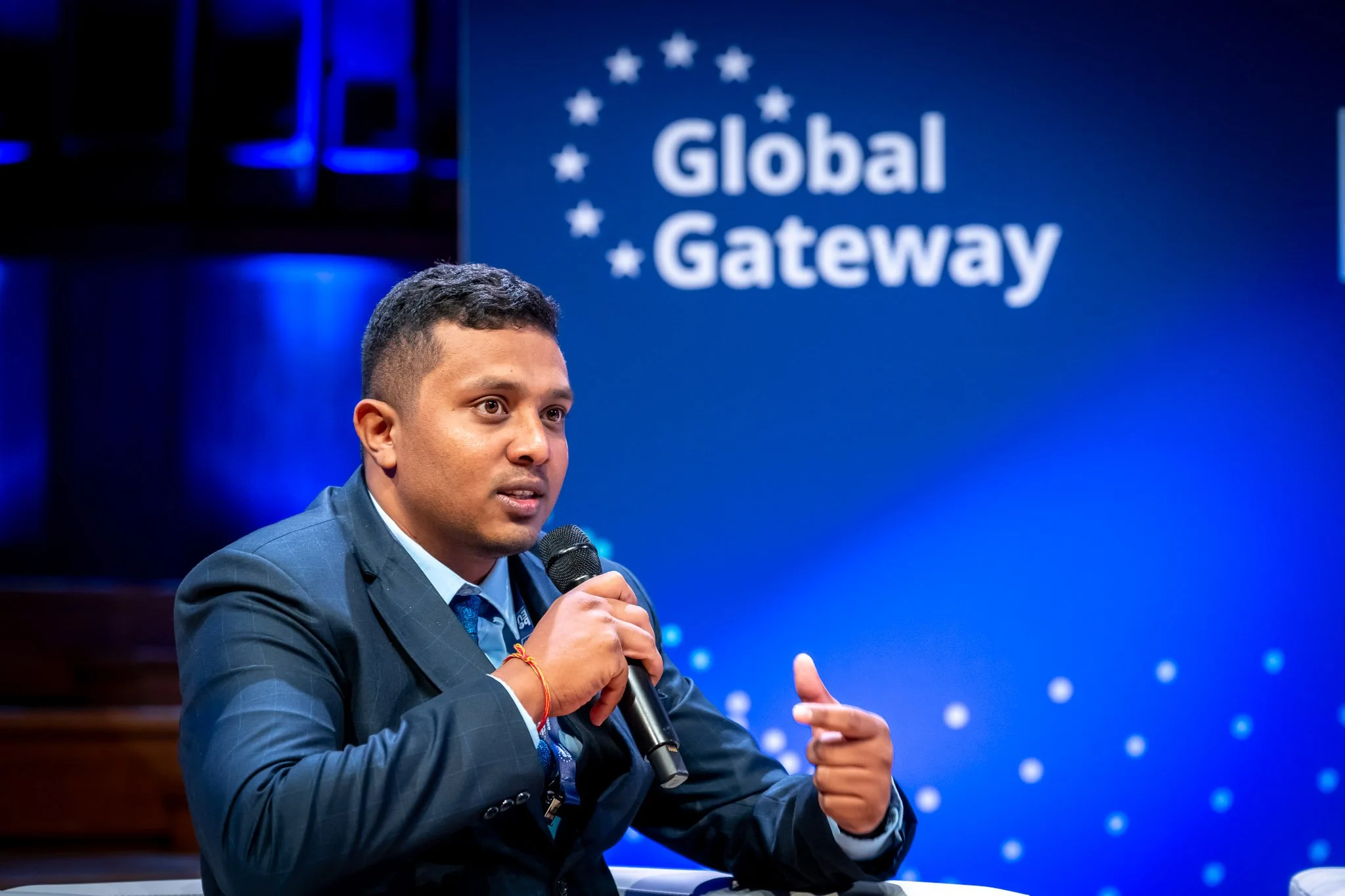 A man in a suit speaking into a microphone at a ‘Global Gateway’ event, against a blue background.